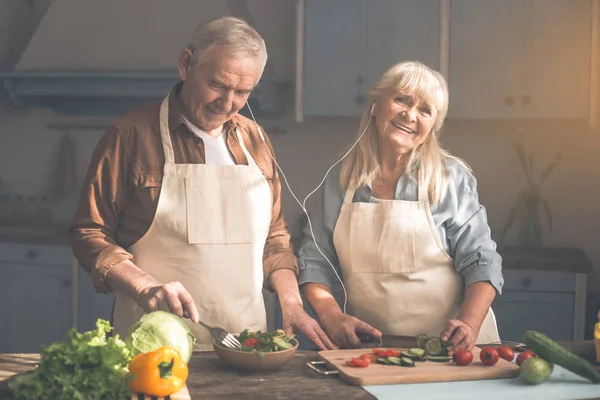 Vrolijke senior man en vrouw genieten van muziek in koken kamer — Stockfoto