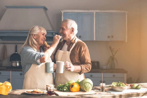 Cheerful senior couple feeding each other by sweet pastry — Stock Photo, Image