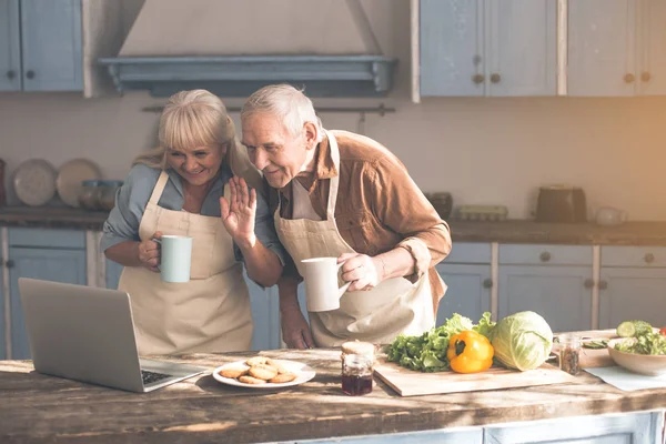 Jubilados jubilados alegres disfrutando de la comunicación en línea en la cocina — Foto de Stock