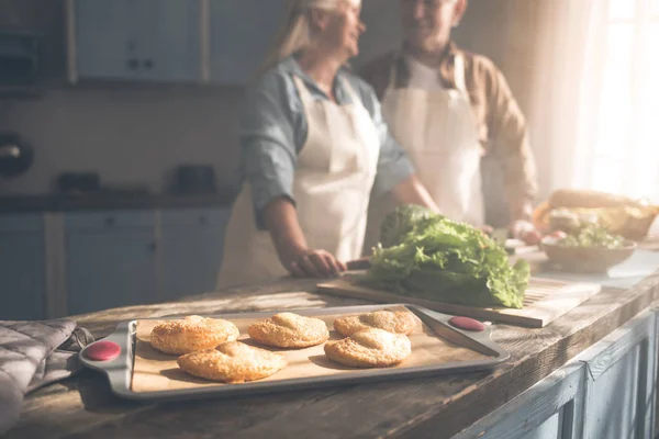 Vrolijke volwassen echtpaar bakken broodjes in koken kamer — Stockfoto