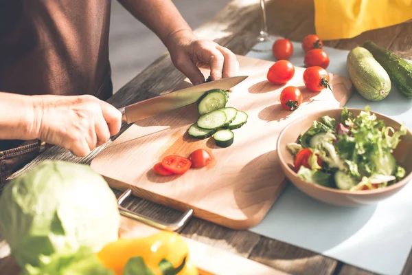 Mature female hands cutting vegetables on wooden board — Stock Photo, Image