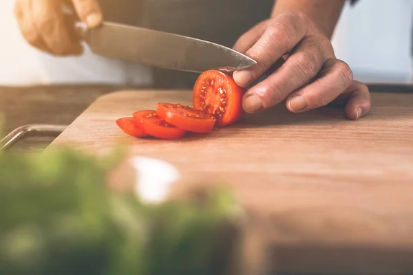 Oude vrouw handen snijden van tomaten op een houten bord — Stockfoto