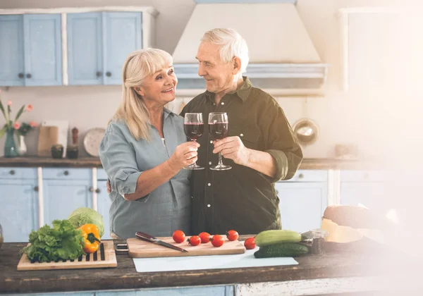 Alegre hombre maduro y mujer tintineo viñas en la cocina — Foto de Stock