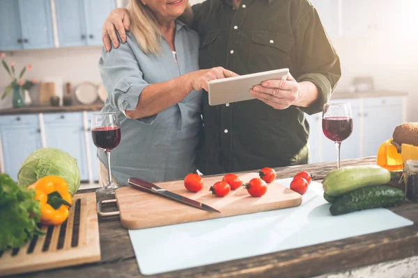Cheerful senior man and woman using tablet in cook room