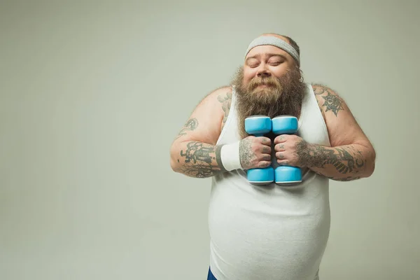 Веселий товстий чоловік робить люблячий хмарочос зі спортивними вагами — стокове фото
