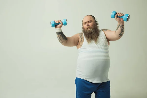 Hombre gordo relajado escuchando música y levantando pesas — Foto de Stock