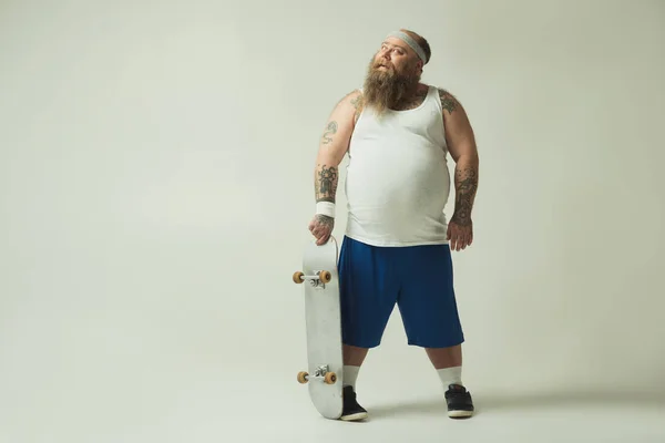 Veselý tlustý muž udržuje skateboard a snění — Stock fotografie