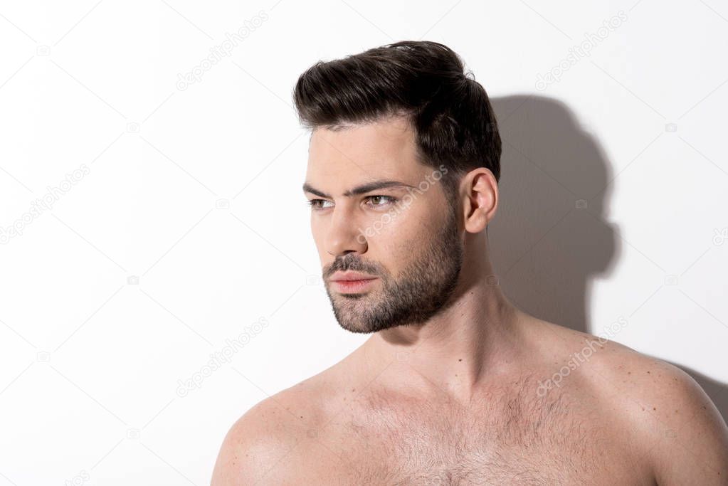 Pensive young man is posing against white wall