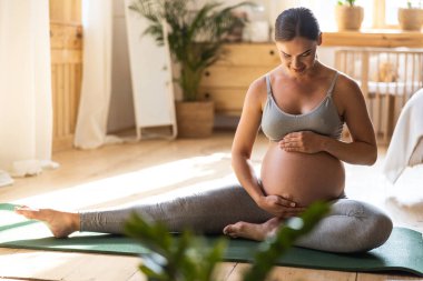 Happy pretty expectant mother sitting on the mat at home
