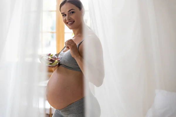 Mujer embarazada sonriente está de pie con ensalada —  Fotos de Stock