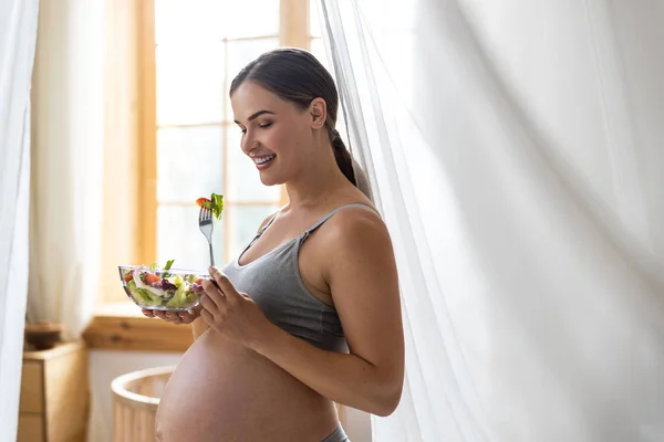 Lächelnde junge werdende Mutter isst Gemüse zu Hause — Stockfoto