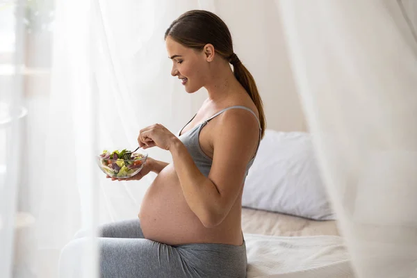 Lächelnde werdende Mutter beim Betrachten ihres Salats — Stockfoto