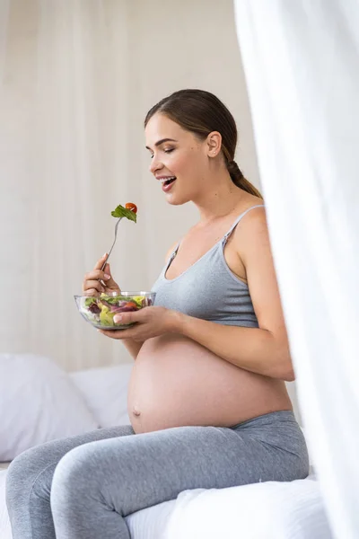 Femme enceinte souriante tenant fourchette aux légumes — Photo