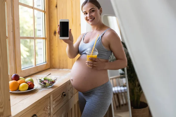 Feliz señora embarazada agradable está mostrando teléfono inteligente —  Fotos de Stock