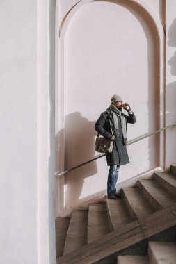 Sabahları sıcak paltolu yetişkin bir adam dışarıda kahve içiyor.