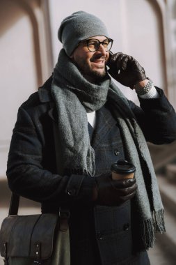 Yetişkin gülümseyen beyaz adam dışarıda cep telefonuyla konuşuyor.