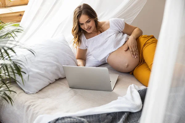 Счастливая беременная женщина печатает на ноутбуке — стоковое фото