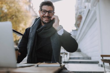 Gözlüklü gülümseyen adam kameraya bakıyor.