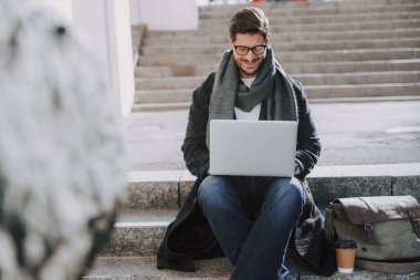 Gözlüklü beyaz adam merdivenlerde oturuyor.