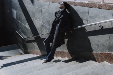 Dışarıdaki merdivenlerde duvara yaslanan sakin adam.