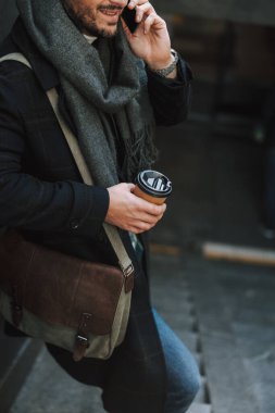 Sıcak kıyafetler içinde gülümseyen ve merdivenlerde çay içen adam.