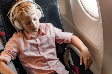 Küçük çocuk uçağın penceresinin yanında uyuyor.