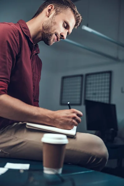 Smiling young man making notes in a notebook at work — Stock Photo, Image