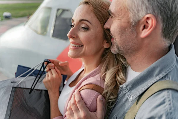 Jolie femme souriante tenant avec des sacs à provisions près de l'avion — Photo