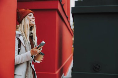 Sıcak içeceği olan bayan öğrenci dışarıda gülüyor.