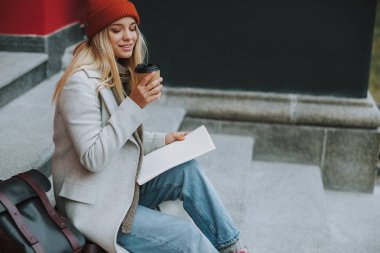 Kitapları olan genç bayan kahvenin tadını çıkarıyor.