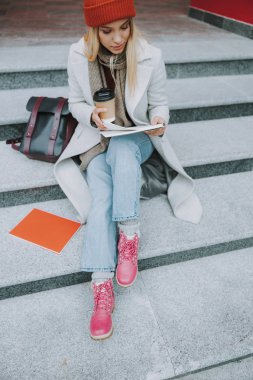 Elinde kitap ve kahve tutan genç bir kız öğrenci.