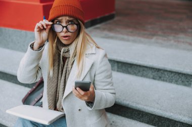 Şok olmuş yüzüyle akıllı telefona bakan bir kız öğrenci.