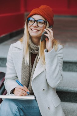 Kitapla akıllı telefondan konuşan genç bir kız öğrenci.