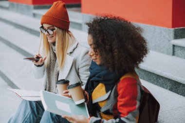 Beyaz ve Afro-Amerikan kadınları akıllı telefonlarıyla birlikte oturuyorlar.