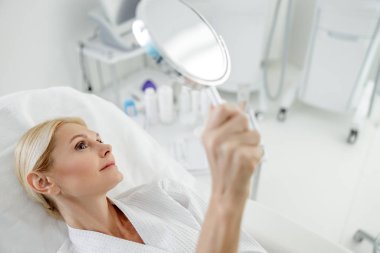 Aynalı beyaz bornozlu çekici bir kadın.