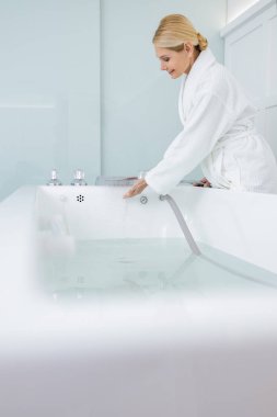 Gülümseyen güzel kadın hidromasaj banyosunda suya bakıyor.