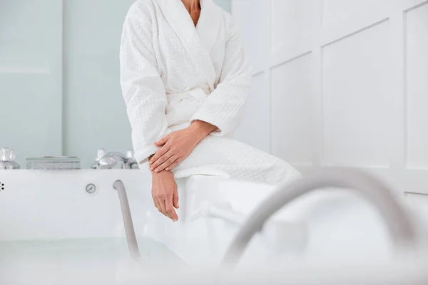 Mujer con albornoz blanco y sentada cerca de la bañera de hidromasaje — Foto de Stock