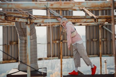 Adam çatıda metal bir yapıya tutunuyor.