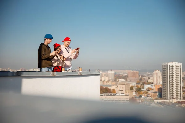 Drie gelukkige vrienden kijken op hun telefoons op het dak — Stockfoto