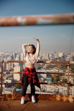 Gülümseyen çekici kız, gözleri kapalı çatıda duruyor.