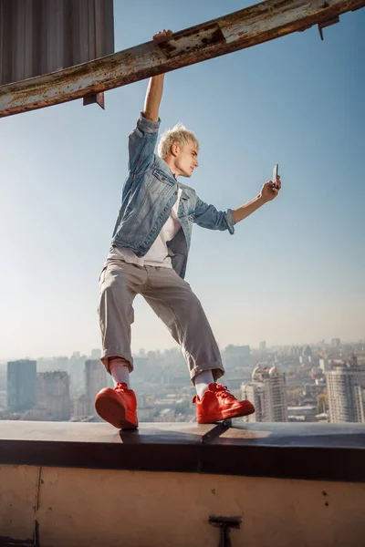 Stylish young guy holding smartphone on the roof — Stock Photo, Image