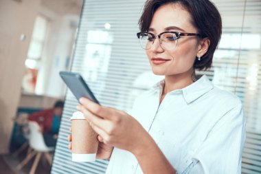 Genç bayan ofisinde akıllı telefondan yazı yazıyor.