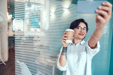 Gülümseyen güzel bayan elinde kahve ve cep telefonu tutuyor.