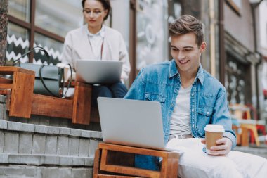 Dışarıda dizüstü bilgisayarla oturan mutlu genç adam.