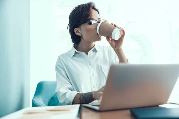 Ung kvinna dricker kaffe på arbetsplatsen — Stockfoto