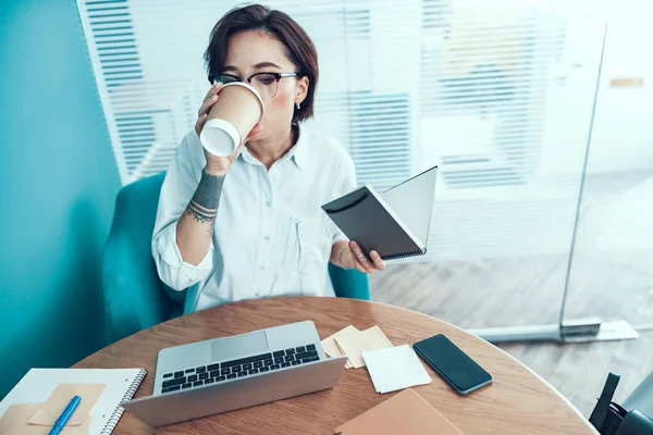 Mujer joven está tomando café en el escritorio — Foto de Stock