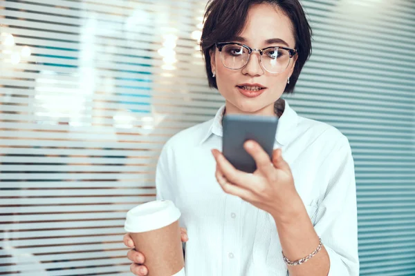 Pretty woman is holding mobile phone in office — Stock Photo, Image