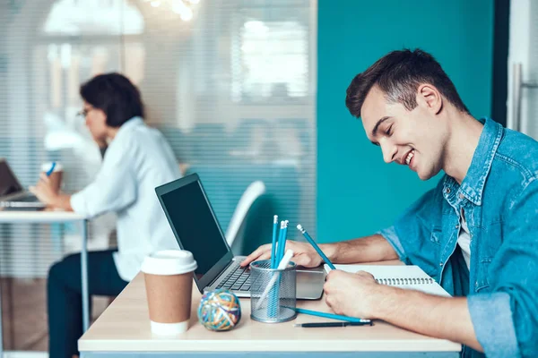 Glücklicher junger Mann schreibt in Notizbuch — Stockfoto