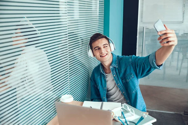 Jeune homme heureux fait selfie sur le lieu de travail — Photo