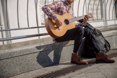 Genç müzisyen oturmuş gitarını tutuyor.